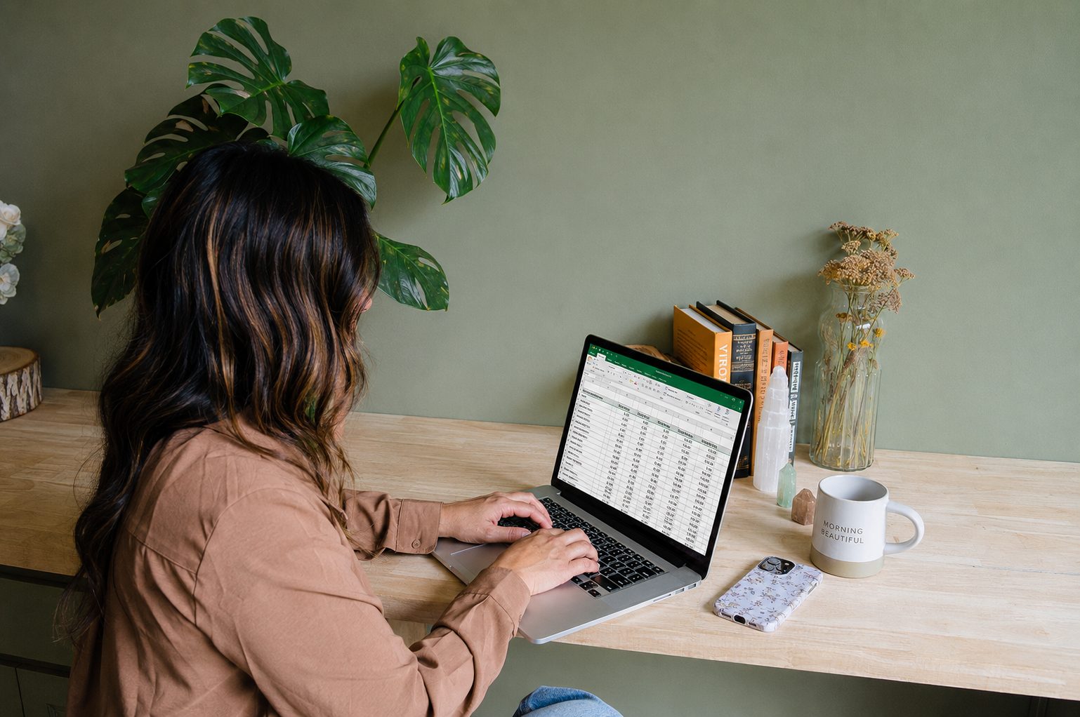 Cate typing on her laptop at a wooden desk beneath a monstera plant